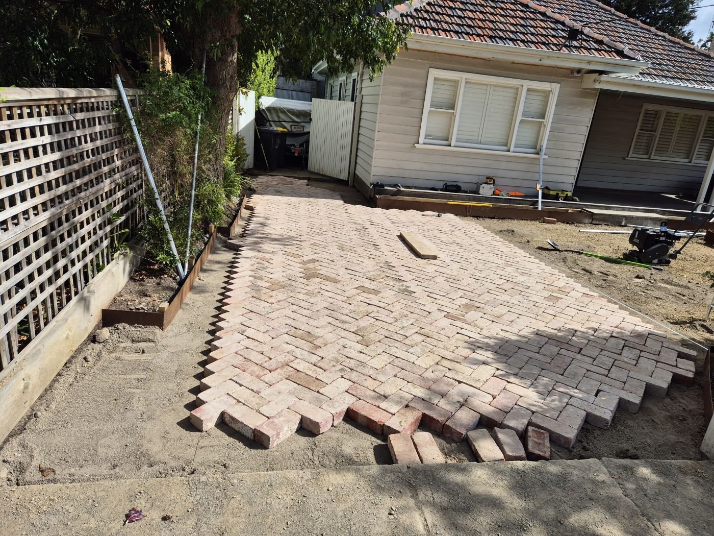 Herringbone brick courtyard half laid in front of a weatherboard home