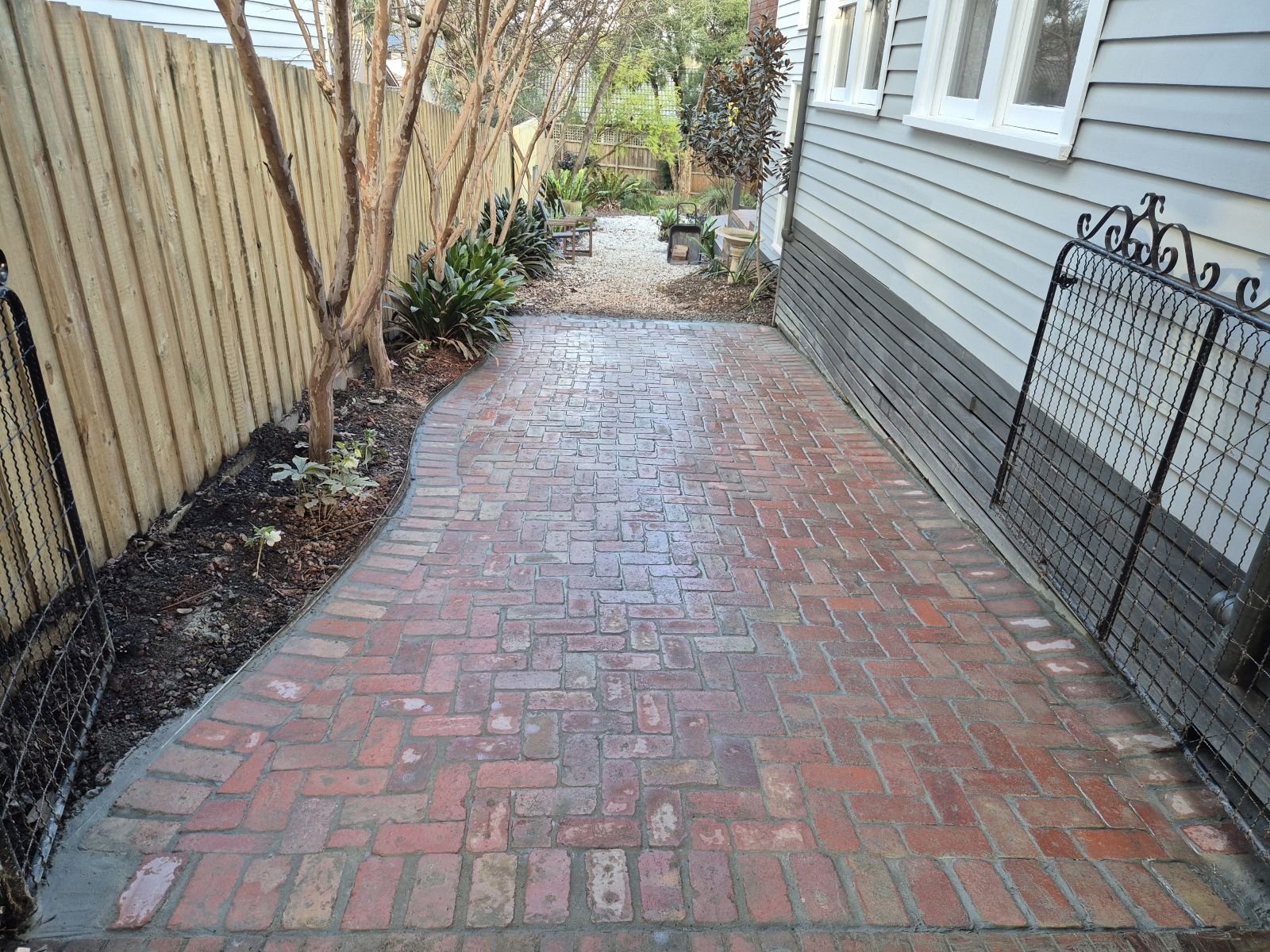 Curved red brick garden path along a weatherboard home