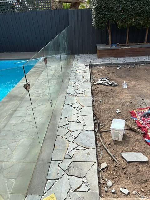 Crazy paving being laid around a pool with glass fencing