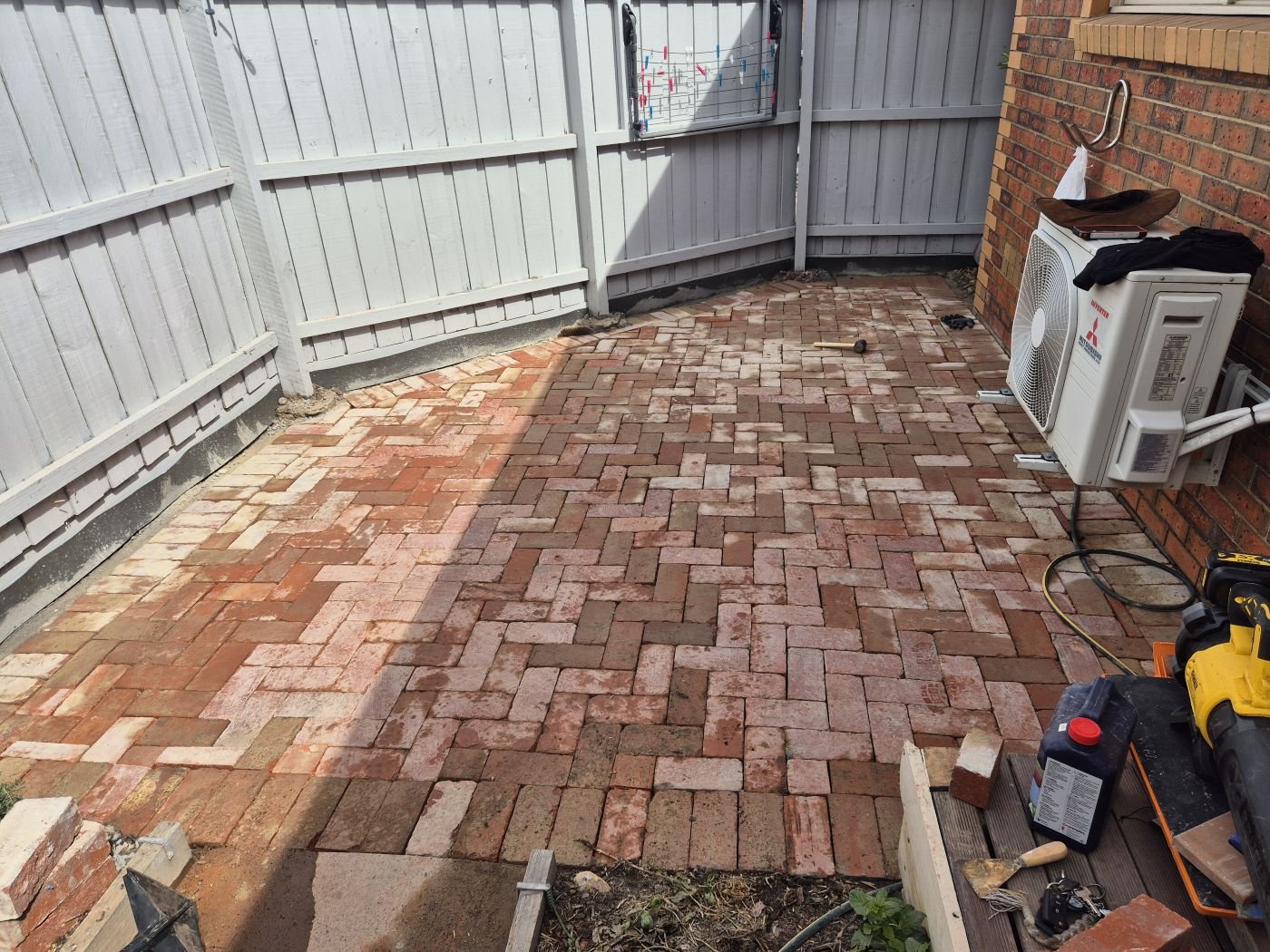 Recycled brick courtyard freshly laid beside a grey fence