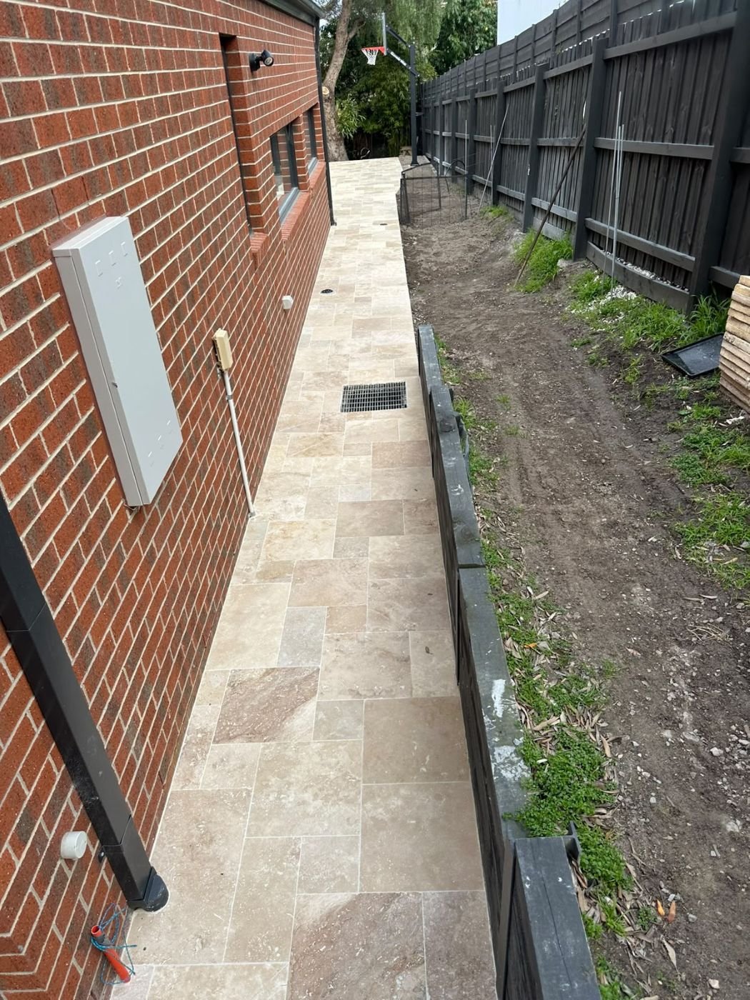 Travertine side path with drainage grate alongside a brick house
